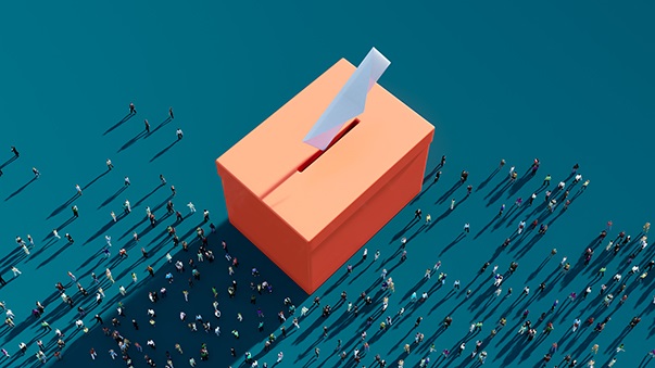 A large orange ballot box surrounded by tiny people.