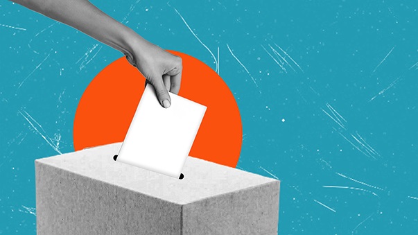 A hand dropping a ballot into a box.