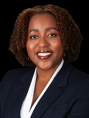 A woman dressed in a business suit and white blouse smiles confidently at the camera.
