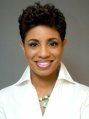 A woman with short hair and glasses wearing a judge's robe with an American flag in the background.