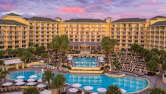 A grand hotel surrounding a pool with palm trees.