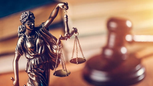 Bronze Lady Justice statue in front of an out-of-focus gavel and sounding block.