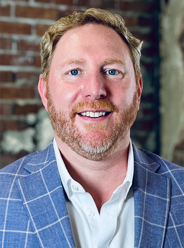 Man with red hair and beard in a blue suit coat and white dress shirt.