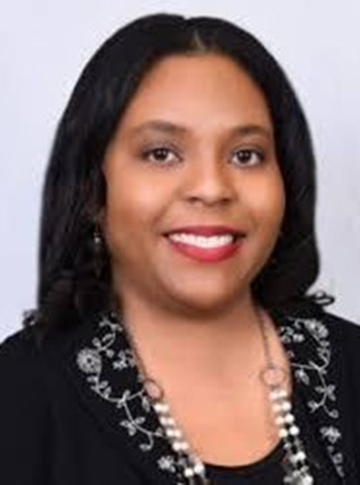 A woman with long black hair wearing a black top with white floral embroidery on the collar and a delicate necklace
