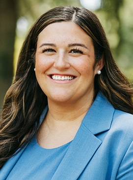 Woman with long brunette hair in a cornflower blue suit and pearl earrings.